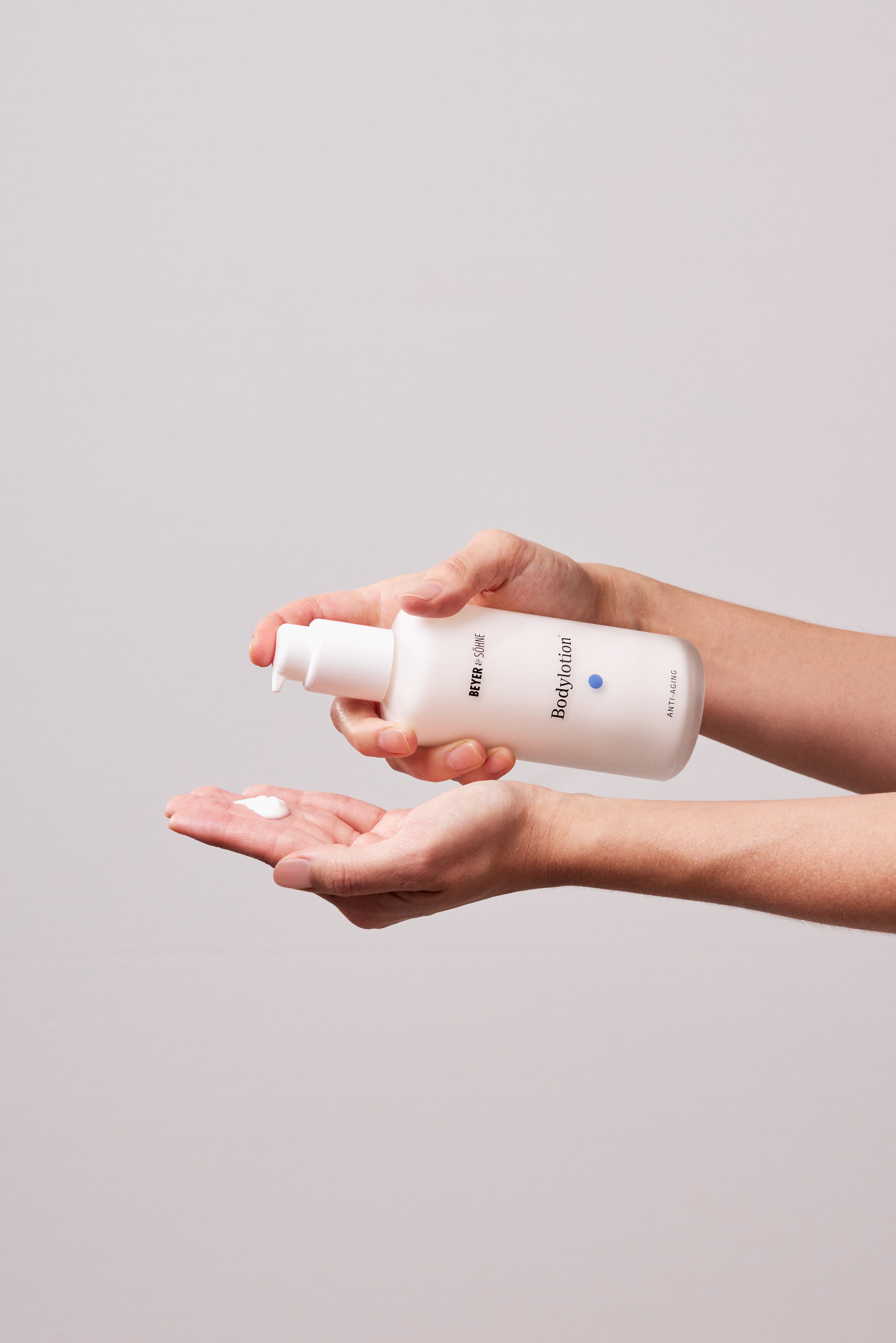 Bodylotion+ von Beyer & Söhne wird in der Hand gehalten und pumpt eine kleine Menge der Creme aus dem Spender auf die andere Hand